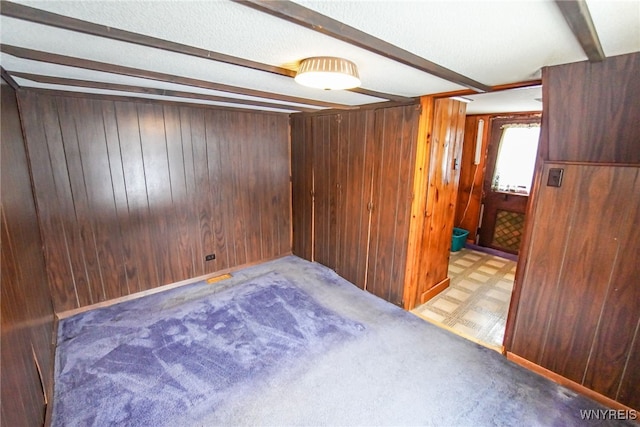 unfurnished room featuring light colored carpet, wooden walls, and beam ceiling