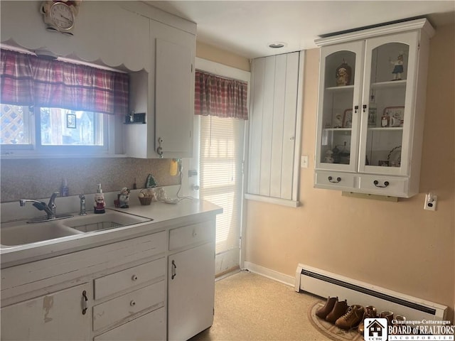 kitchen with a wealth of natural light, a baseboard heating unit, sink, and white cabinets