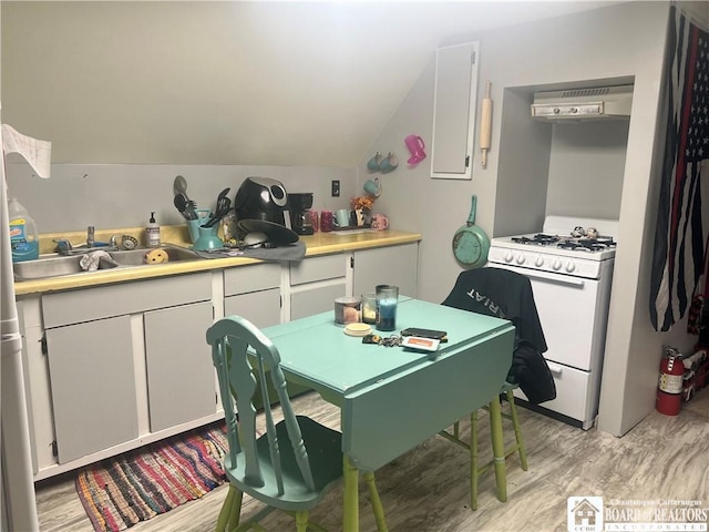 kitchen with lofted ceiling, white range with gas stovetop, white cabinets, exhaust hood, and light wood-type flooring