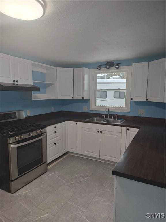 kitchen featuring dark countertops, under cabinet range hood, stainless steel gas stove, white cabinets, and a sink