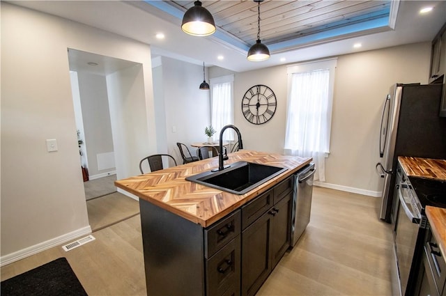 kitchen with sink, wooden counters, hanging light fixtures, a tray ceiling, and a center island with sink