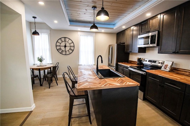 kitchen featuring stainless steel appliances, pendant lighting, a center island with sink, and a tray ceiling