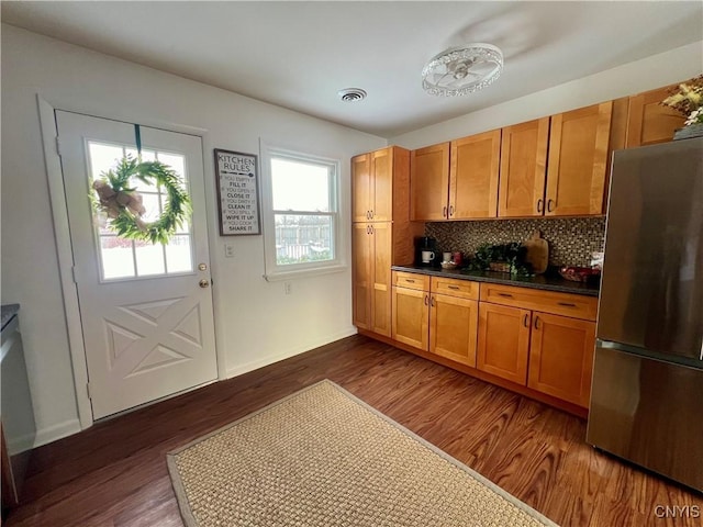 kitchen featuring dark hardwood / wood-style flooring, backsplash, and stainless steel refrigerator