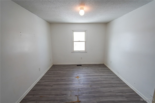 empty room with dark hardwood / wood-style floors and a textured ceiling