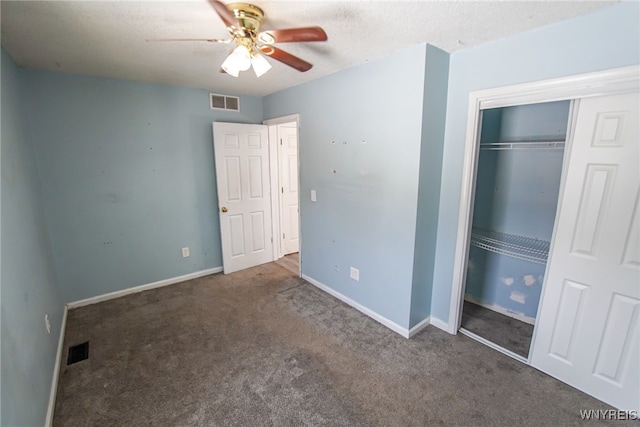 unfurnished bedroom with ceiling fan, a textured ceiling, a closet, and dark colored carpet