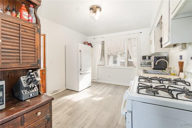 kitchen with white cabinetry, sink, white appliances, and light hardwood / wood-style flooring