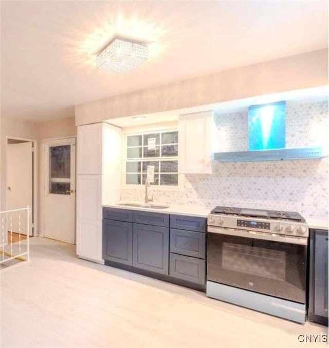 kitchen featuring a sink, white cabinets, light countertops, stainless steel range with gas cooktop, and wall chimney exhaust hood