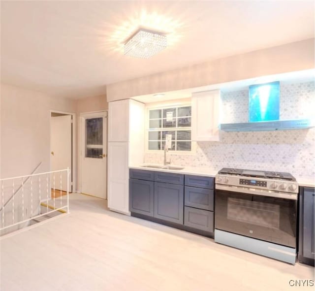 kitchen with stainless steel range with gas cooktop, light countertops, a sink, and wall chimney range hood