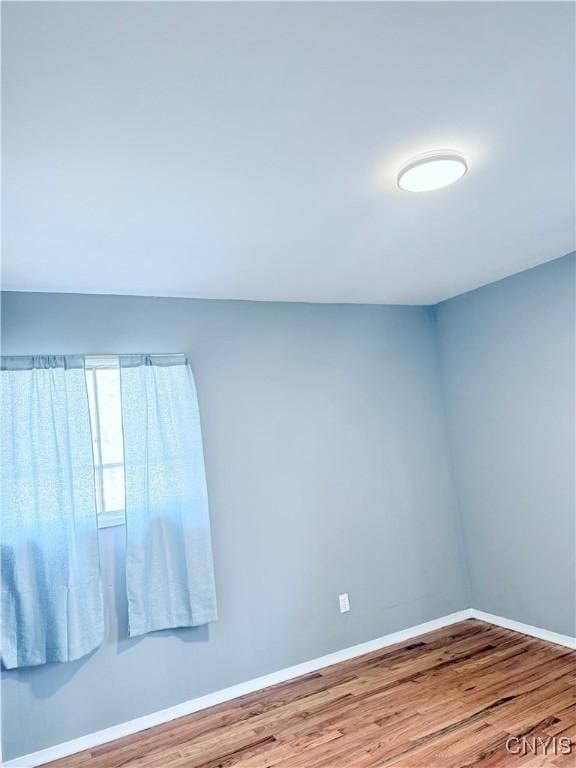 spare room with baseboards and wood finished floors