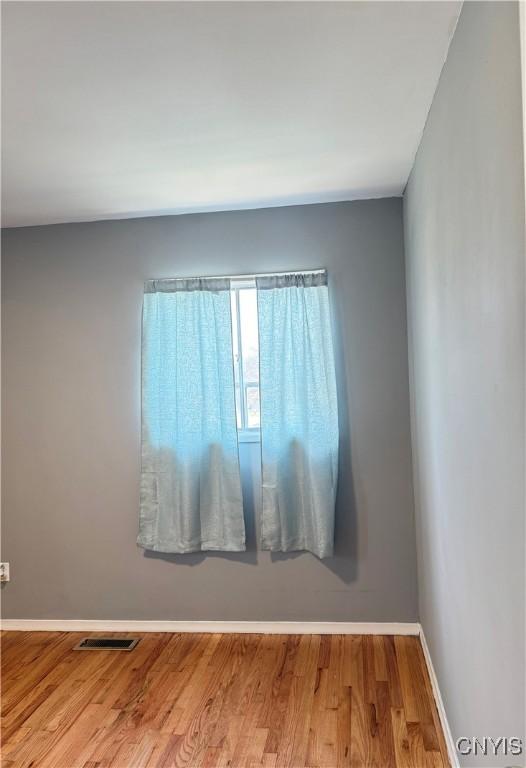 empty room featuring wood finished floors, visible vents, and baseboards