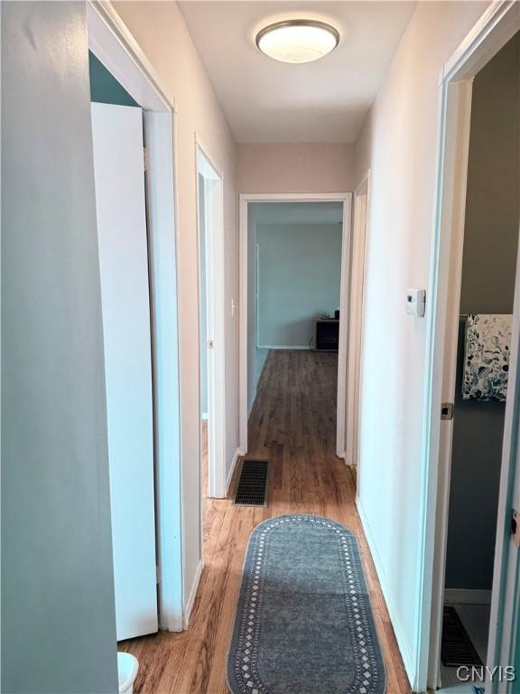 hallway featuring visible vents, light wood-type flooring, and baseboards