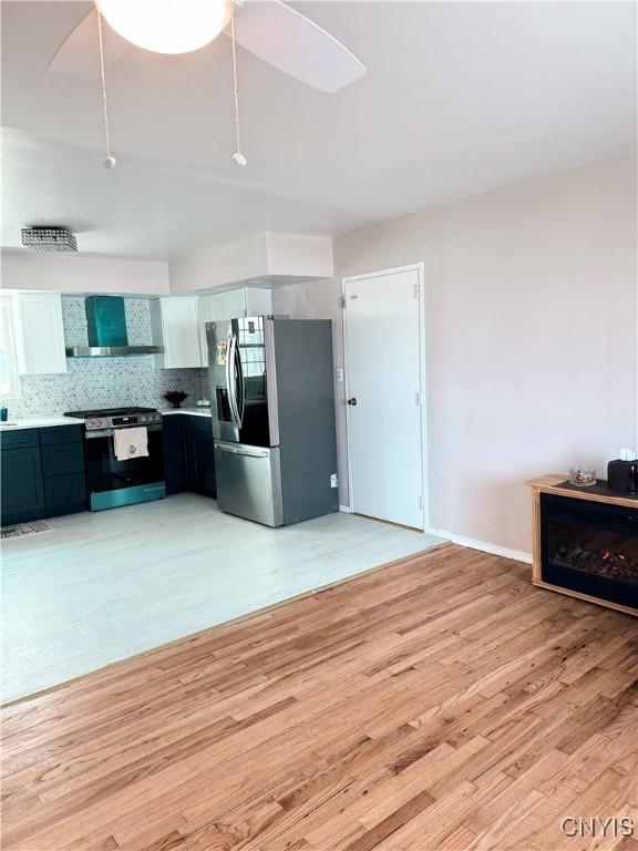 kitchen with stainless steel refrigerator with ice dispenser, electric stove, light wood-style floors, wall chimney exhaust hood, and decorative backsplash