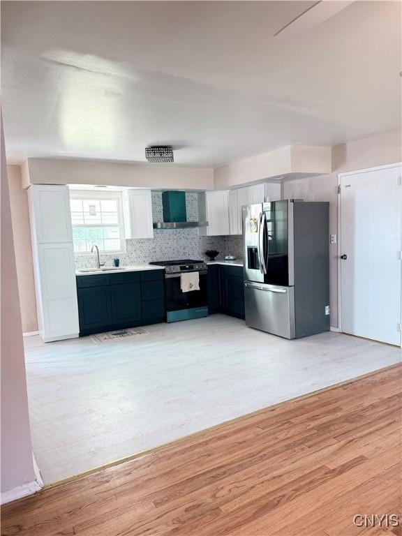 kitchen with wall chimney range hood, stainless steel fridge with ice dispenser, gas range oven, light wood-style flooring, and a sink