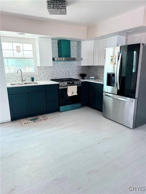 kitchen with a sink, wall chimney range hood, appliances with stainless steel finishes, light countertops, and decorative backsplash