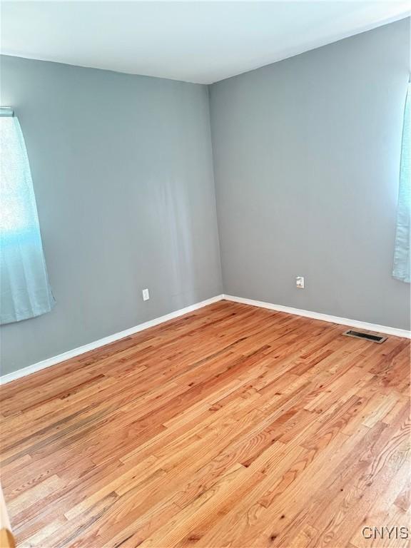 unfurnished room with light wood finished floors, visible vents, and baseboards