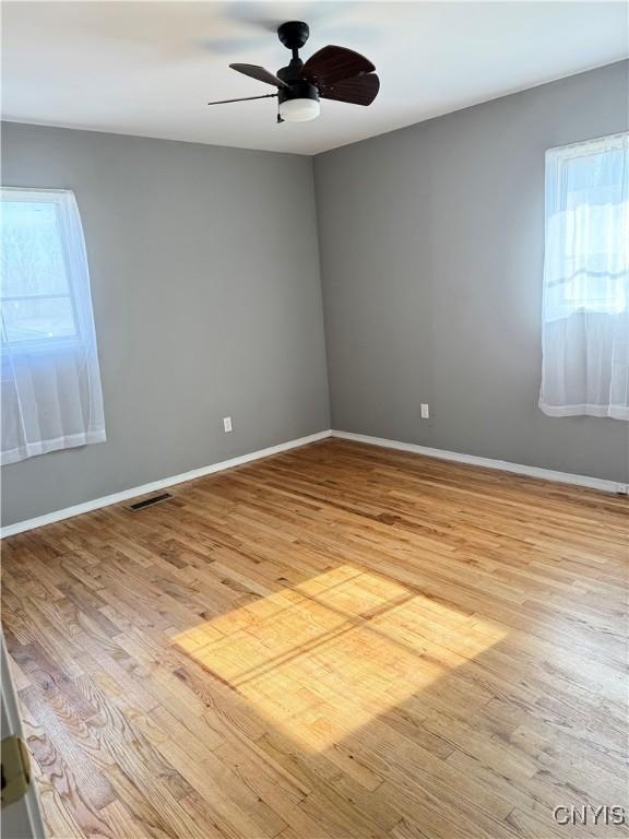 empty room featuring visible vents, a healthy amount of sunlight, light wood-type flooring, and ceiling fan