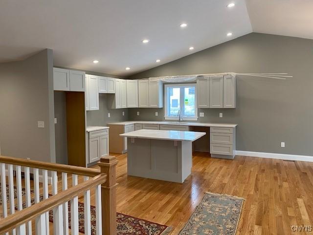 kitchen featuring sink, a center island, white cabinets, vaulted ceiling, and light wood-type flooring