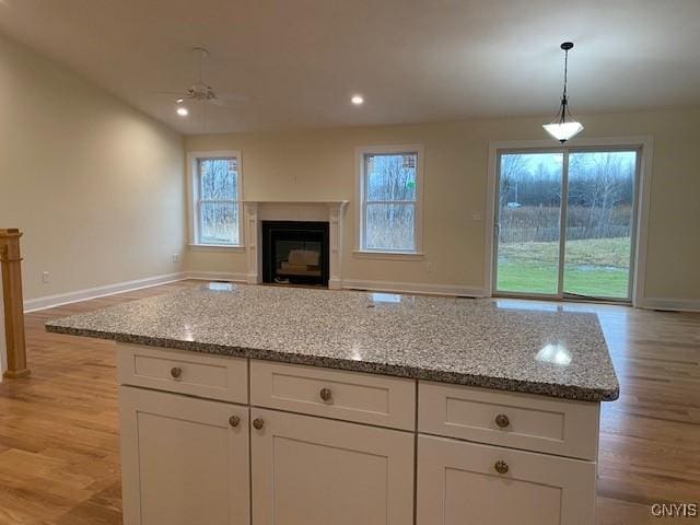 kitchen with pendant lighting, light stone counters, light hardwood / wood-style floors, and white cabinets