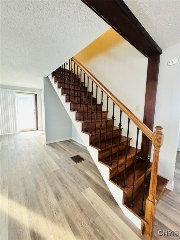 staircase with hardwood / wood-style flooring, beam ceiling, and a textured ceiling