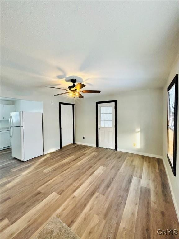 unfurnished bedroom with white fridge, ceiling fan, and light hardwood / wood-style flooring