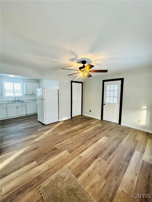 unfurnished bedroom featuring sink, light hardwood / wood-style flooring, a textured ceiling, white refrigerator, and ceiling fan