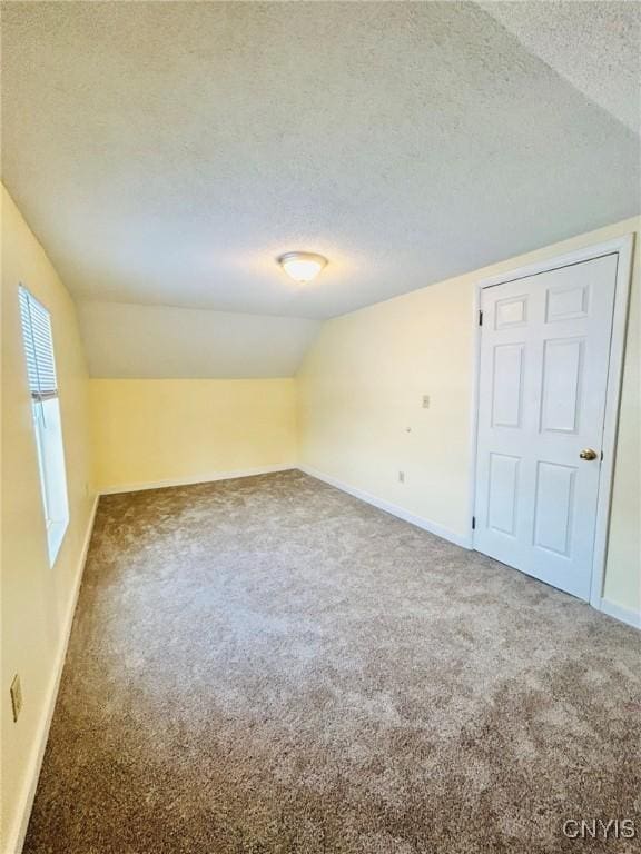 carpeted spare room featuring vaulted ceiling and a textured ceiling