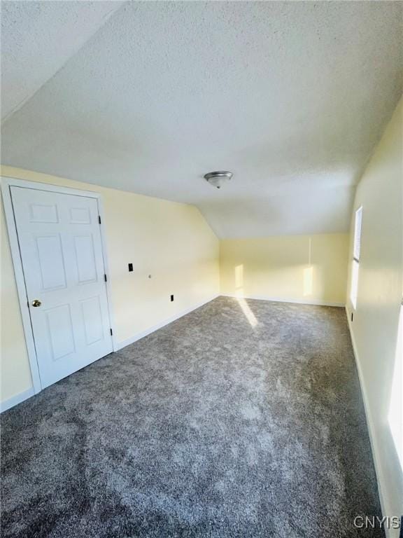 bonus room with vaulted ceiling, dark carpet, and a textured ceiling