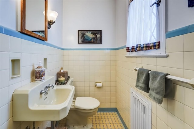 bathroom featuring sink, radiator heating unit, tile walls, and toilet