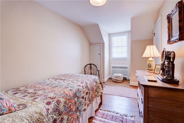 bedroom with vaulted ceiling, dark hardwood / wood-style floors, and radiator heating unit