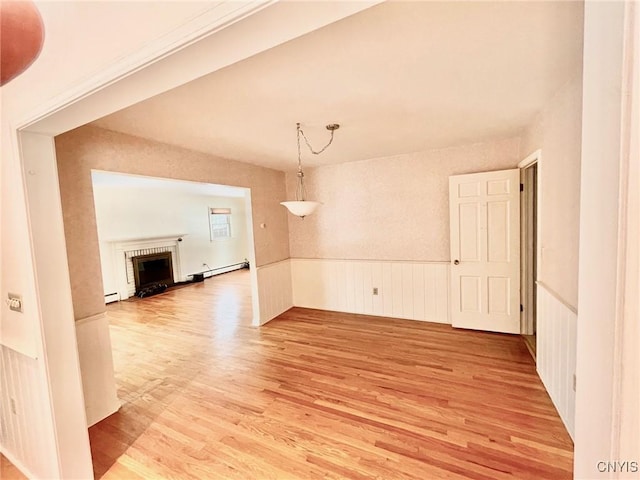 unfurnished room with a baseboard radiator, a brick fireplace, and light wood-type flooring