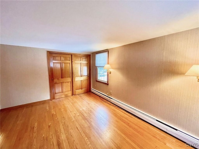 unfurnished bedroom with a baseboard heating unit and light hardwood / wood-style floors