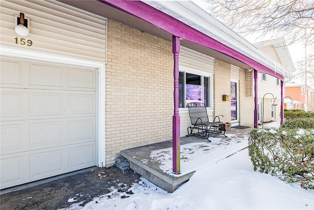 snow covered property entrance with a garage and a porch