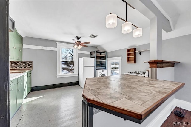 kitchen featuring white fridge, pendant lighting, green cabinets, and backsplash