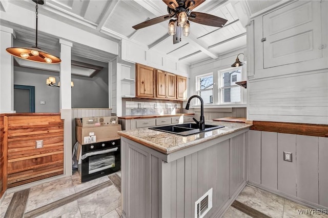 kitchen featuring pendant lighting, sink, ceiling fan, light stone countertops, and beamed ceiling