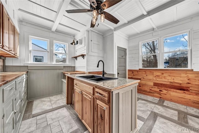 kitchen featuring sink, wooden walls, beamed ceiling, and ceiling fan