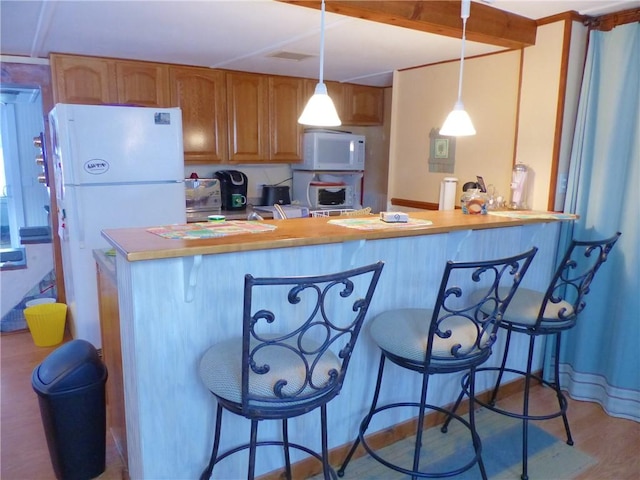 kitchen with decorative light fixtures, white appliances, a breakfast bar area, and kitchen peninsula