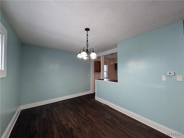 empty room with dark hardwood / wood-style floors, a notable chandelier, and a textured ceiling