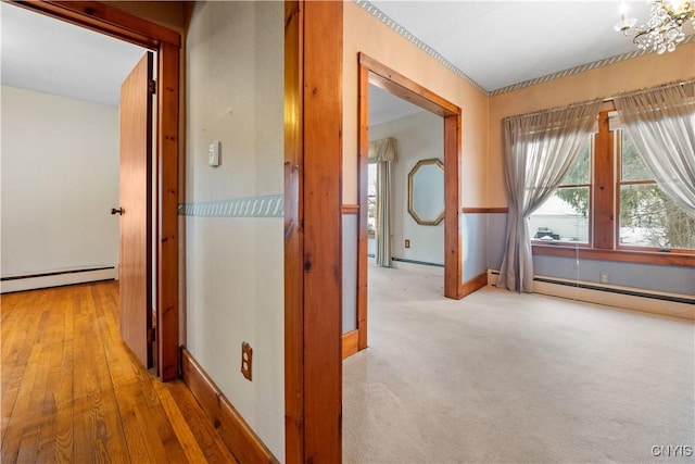 hall featuring a baseboard heating unit, light colored carpet, and a chandelier