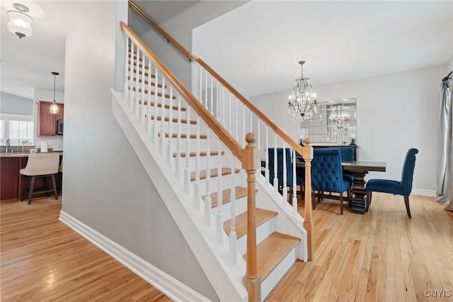 staircase featuring an inviting chandelier, wood-type flooring, and sink