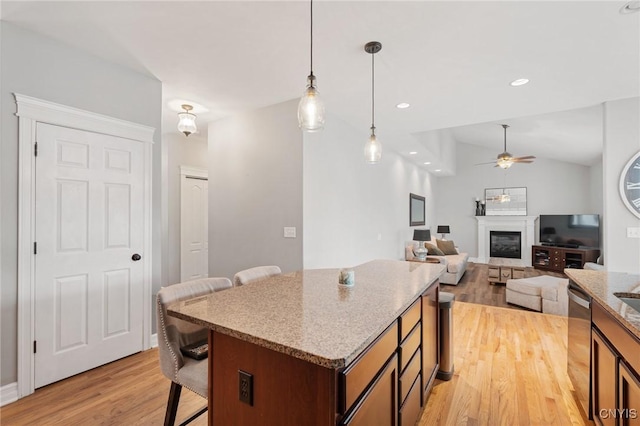 kitchen featuring decorative light fixtures, vaulted ceiling, light hardwood / wood-style flooring, dishwasher, and light stone countertops