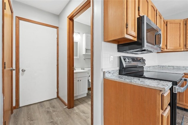 kitchen featuring tasteful backsplash, light hardwood / wood-style flooring, light stone countertops, and appliances with stainless steel finishes