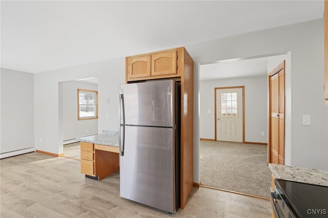 kitchen with light stone counters, light hardwood / wood-style flooring, light brown cabinets, stainless steel refrigerator, and baseboard heating