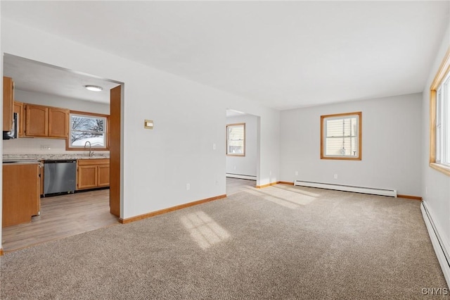 unfurnished living room with baseboard heating, a healthy amount of sunlight, and light carpet