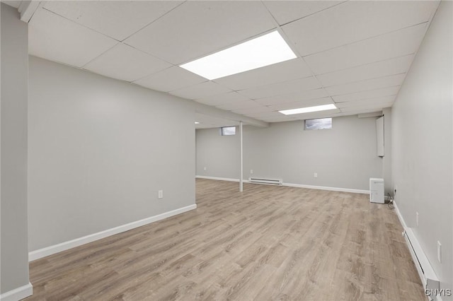 basement featuring a baseboard radiator, light hardwood / wood-style floors, and a drop ceiling