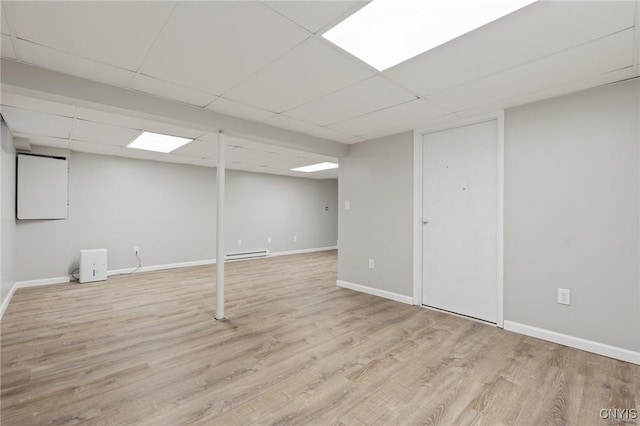 basement featuring light wood-type flooring, a paneled ceiling, and baseboard heating