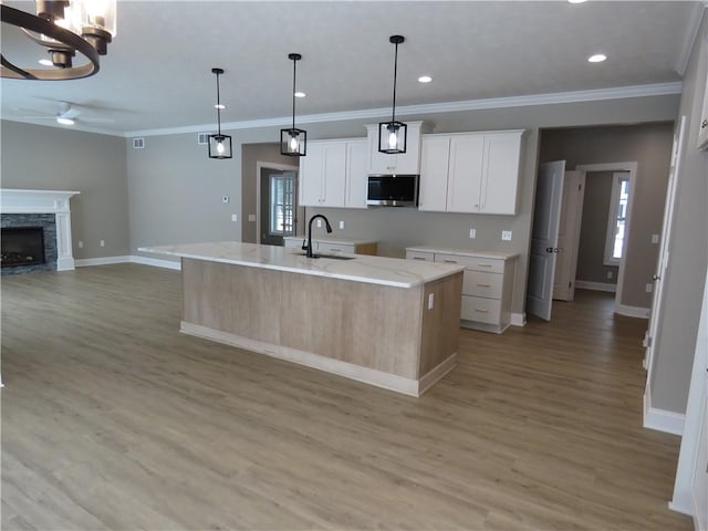 kitchen featuring a stone fireplace, sink, hanging light fixtures, a kitchen island with sink, and white cabinets