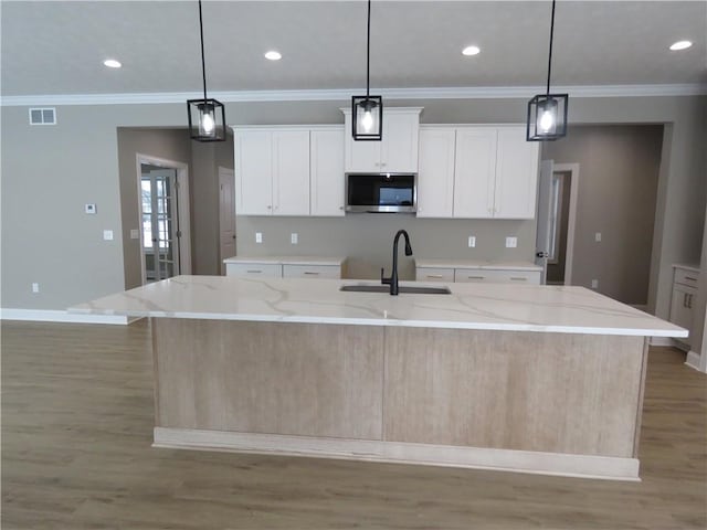 kitchen with a kitchen island with sink, sink, white cabinetry, and hanging light fixtures