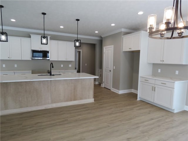 kitchen featuring sink, white cabinetry, light hardwood / wood-style floors, an island with sink, and decorative light fixtures