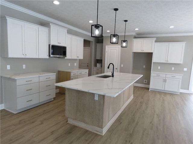 kitchen with sink, light stone countertops, white cabinets, a center island with sink, and decorative light fixtures