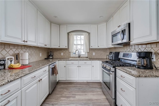 kitchen featuring sink, appliances with stainless steel finishes, backsplash, light stone countertops, and white cabinets